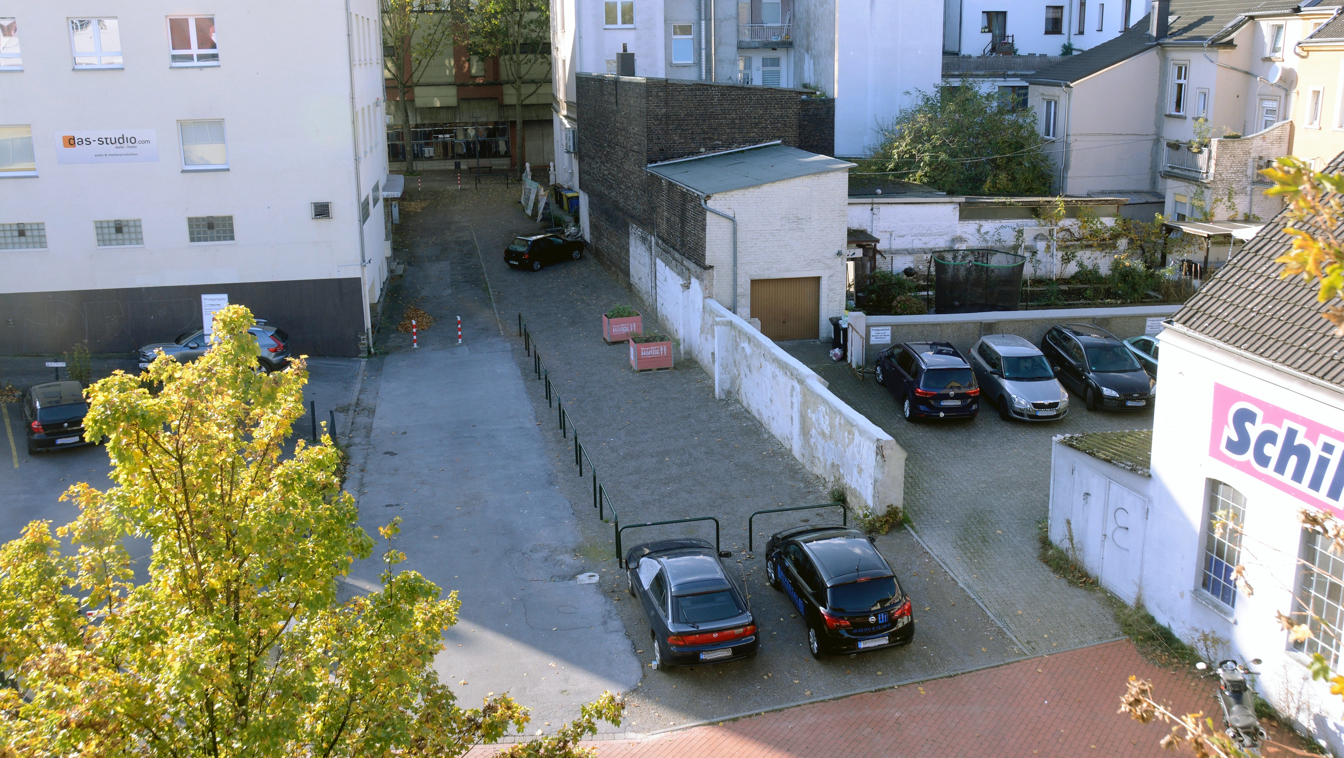 Foto aus der Vogelperspektive von asphaltierter Fläche mit Absperrbügeln vor einer Mauer.
