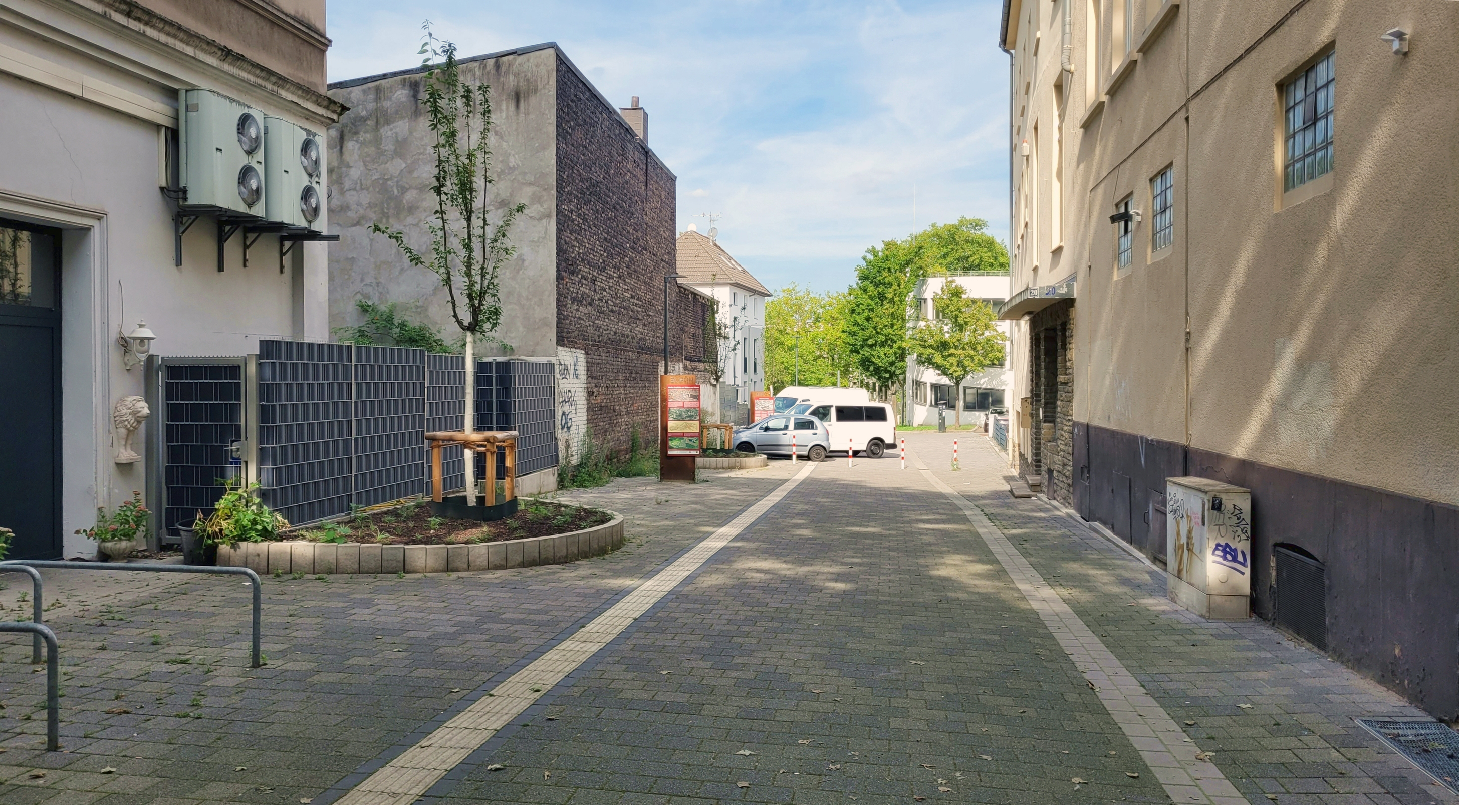 Foto eines schmalen Durchgangs zwischen Gebäuden mit neuem Kopfsteinplfaster und einem frisch geplfanzten Baum.