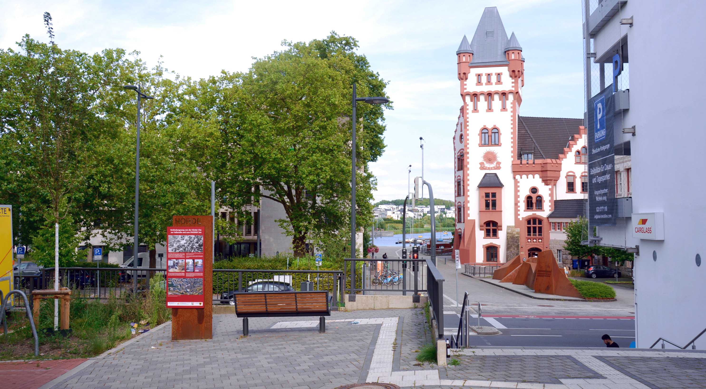 Foto mit freiem Blick auf die Hörder Burg in einiger Entfernung mit einem Fußweg, einer Sitzbank und einer Infostele im Vordergrund.