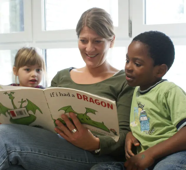 Eine Frau liest einem Jungen und einem Mädchen ein Bilderbuch mit dem Titel "If I had a dragon" vor