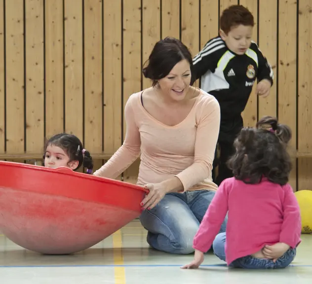 Eine Frau spielt mit drei Kindern in der Turnhalle