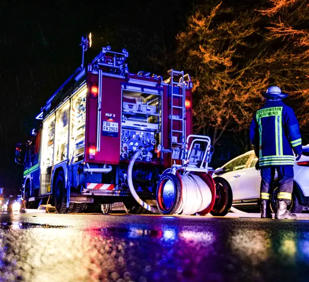 Ein Leiterwagen und ein Feuerwehrmann auf einer nassen Straße im Dunkeln