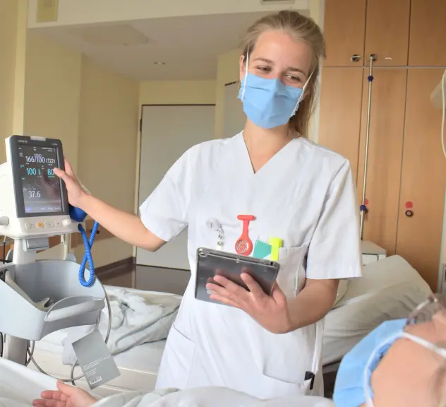 Eine Pflegekraft steht vor einem Krankenbett und überwacht eine Patientin über einen Monitor