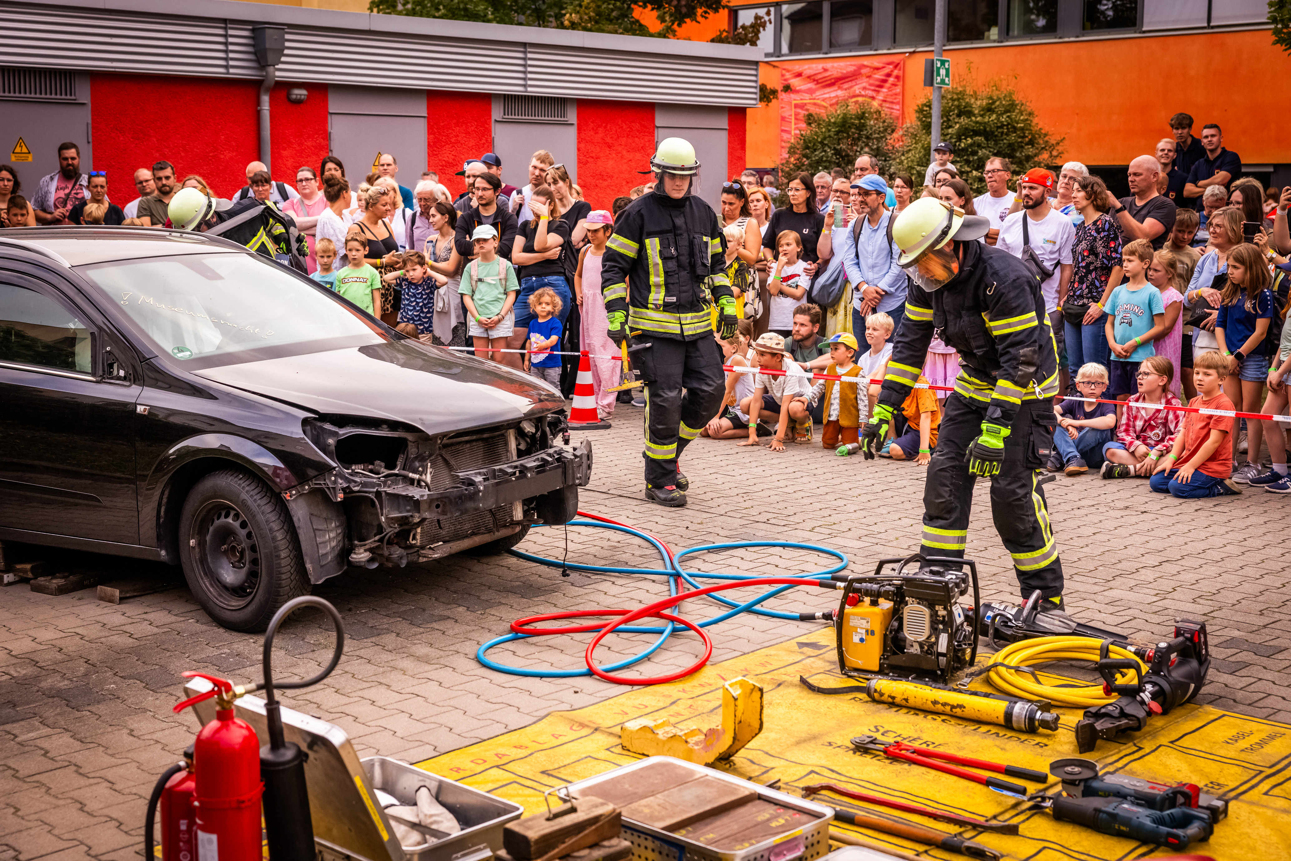Besucher*innen schauen sich eine Vorführung der Feuerwehr Dortmund an. Feuerwehrleute in Berufskleidung arbeiten an einem Auto.