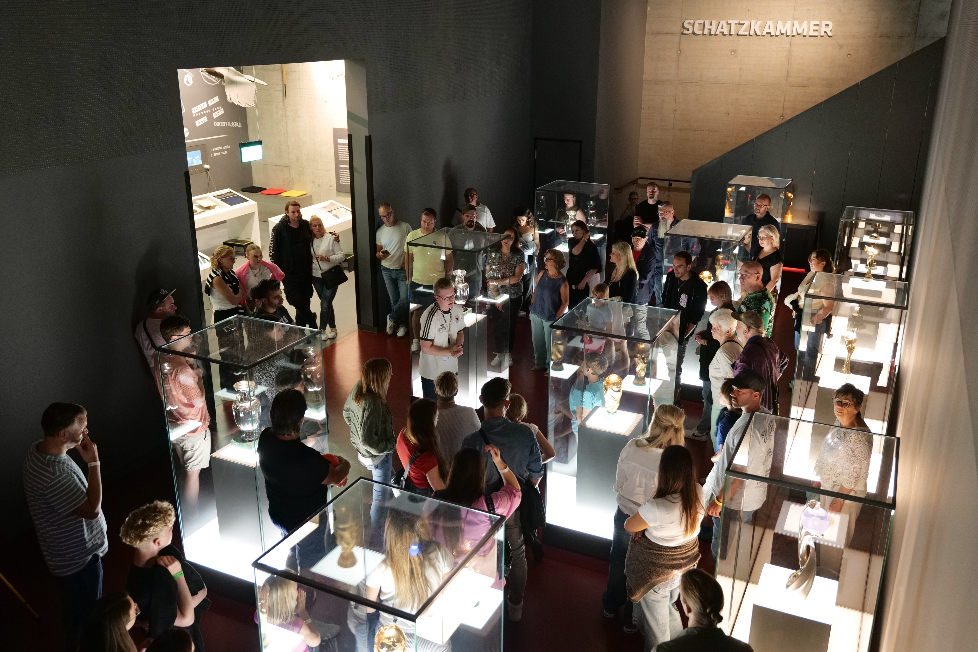 Ausstellungsraum im Deutschen Fußballmuseum mit zahlreichen Vitrinen und Besucher*innen, die sich umsehen.
