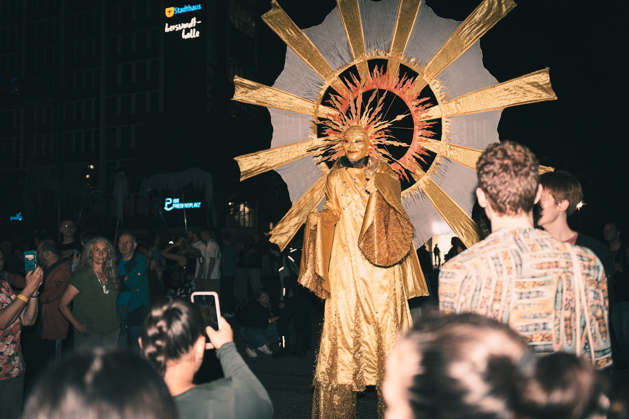 Walk-Act Sonnengestalt. Person in Sonnenkostüm auf Stelzen in der Mitte einer Menschenmenge