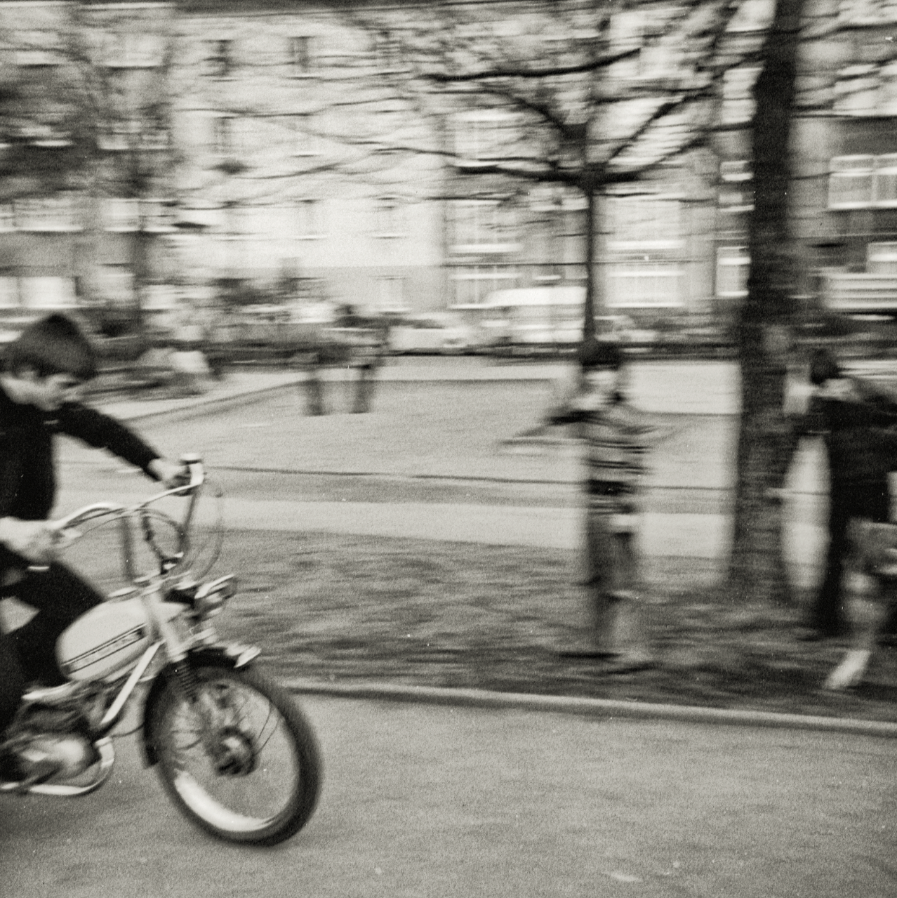 Verzerrtes schwarz-weiß Foto eines Jugendlichen, der Motorrad fährt. Im Hintergrund sind Häuser und Bäume zu sehen.
