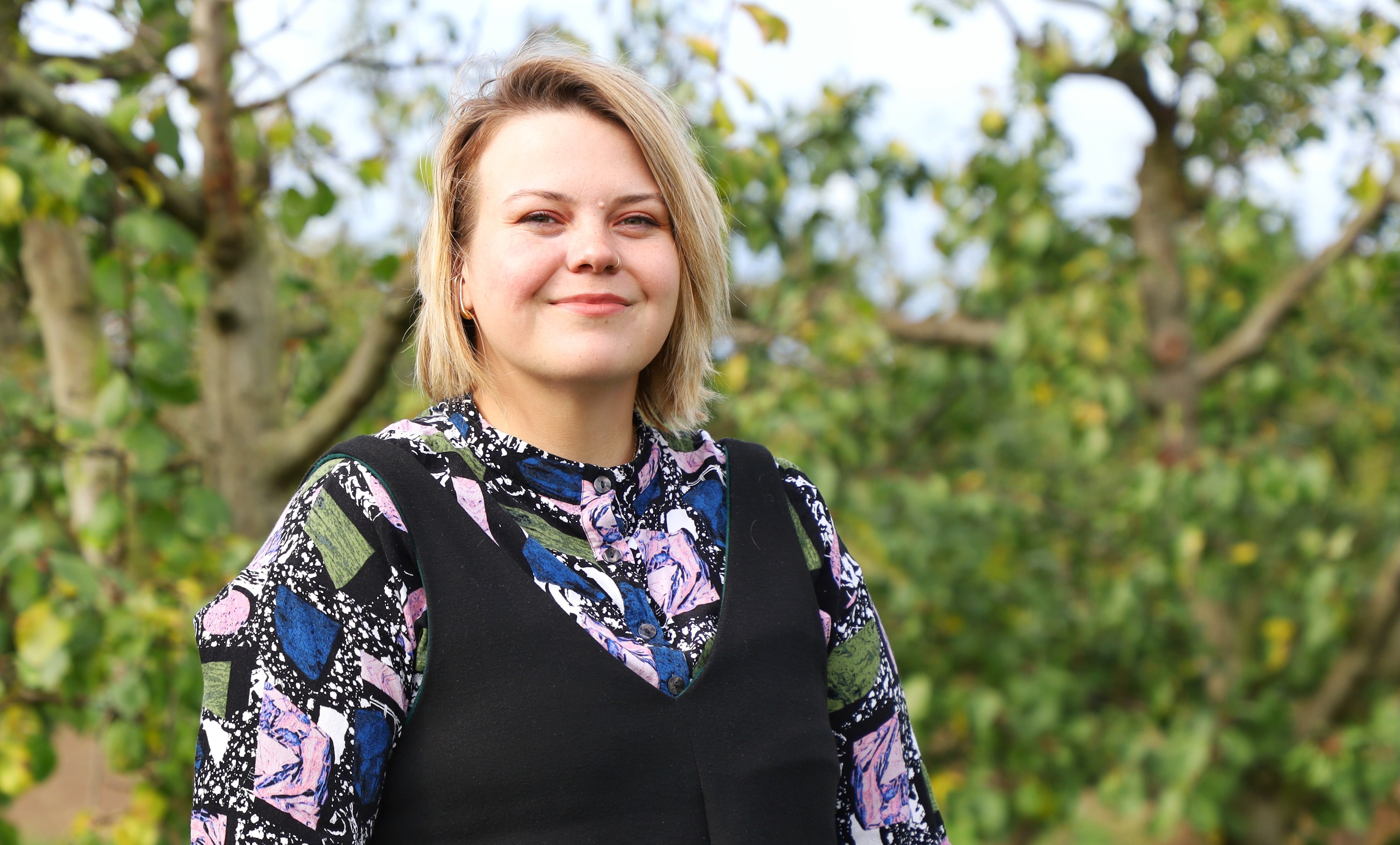 Eine blonde Frau blickt lächeln in die Kamera. 