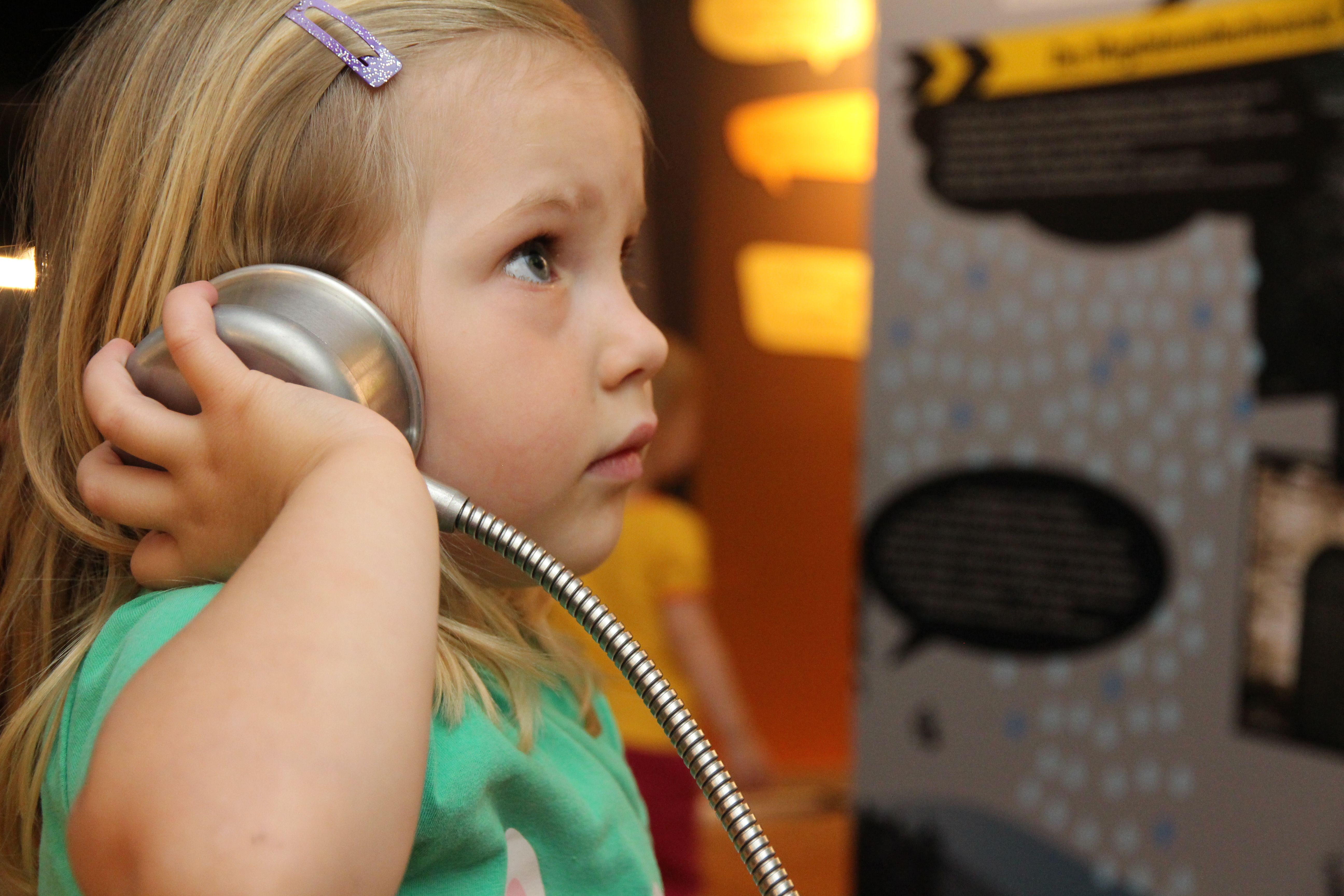 Ein kleines Mädchen hält sich einen Hörknubbel ans Ohr. 