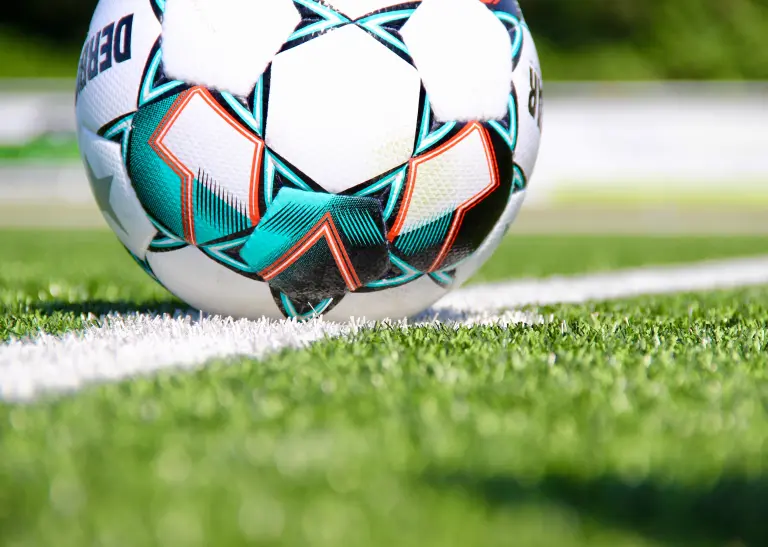 Ein Fußball liegt auf dem Anstoßpunkt eines Kunstrasenspielfeldes.