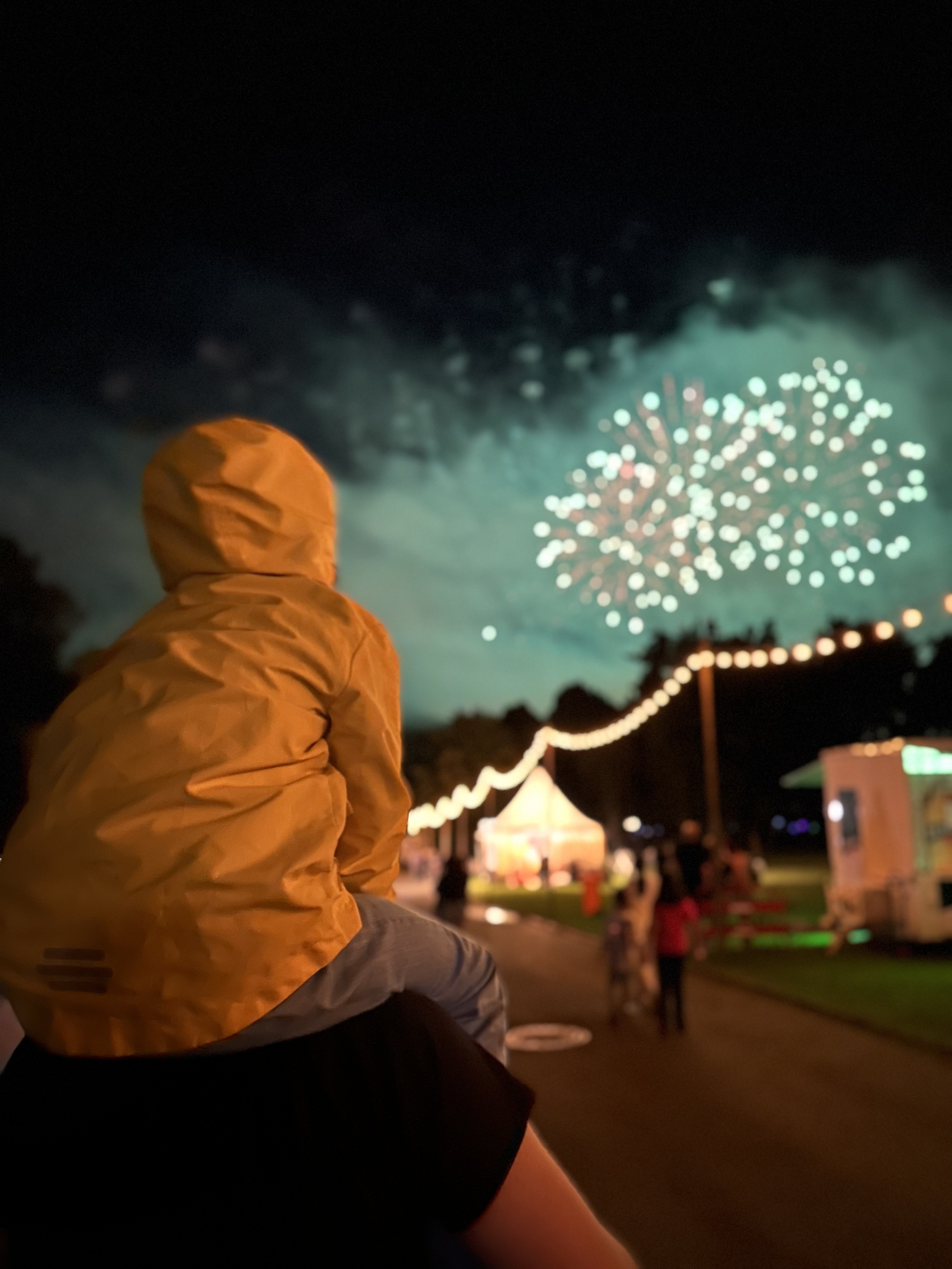 Ein Kind sitzt auf den Schultern von seinem Vater und schaut das Feuerwerk beim Lichterfest an.