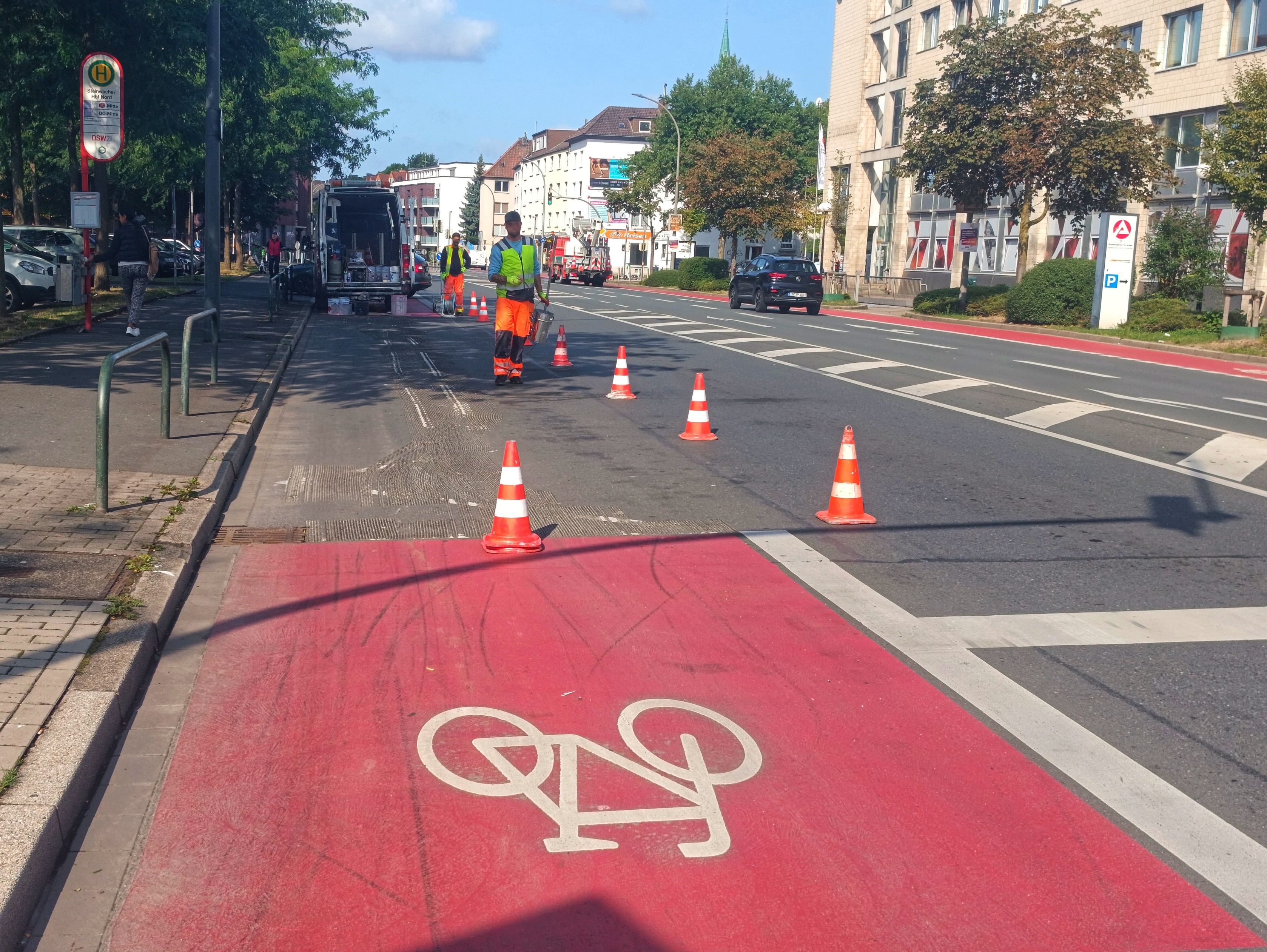 Markierungsarbeiten an einem roten Radfahrstreifen.Hütchen werden von Bauarbeiten aufgestellt.
