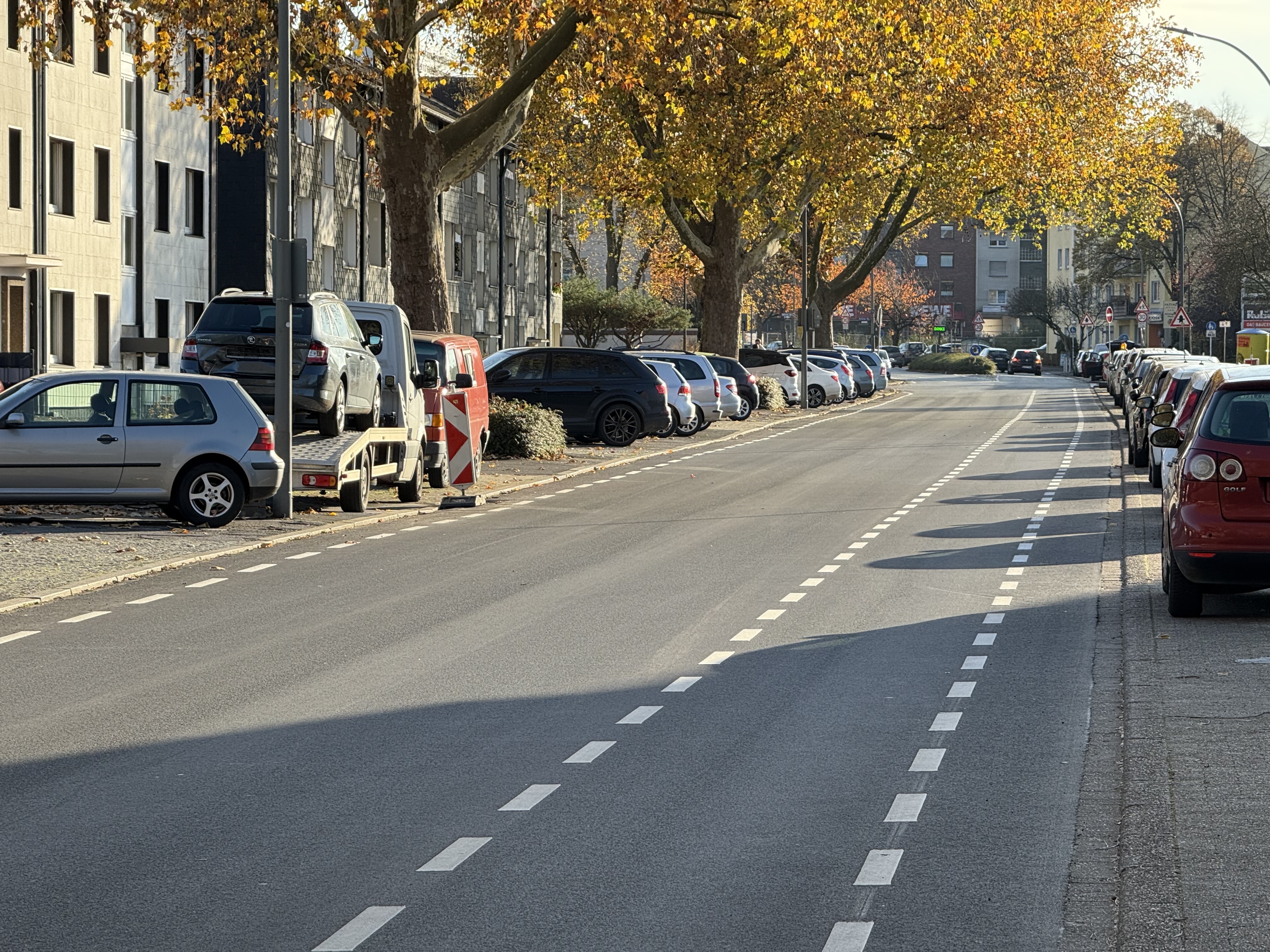 Eine Straße mit einem Fahrradschutzstreifen. Links und rechts parken Fahrzeuge. 