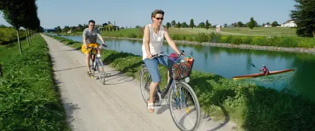 Zwei Personen fahren mit dem Fahrrad neben dem Kanal entlang.