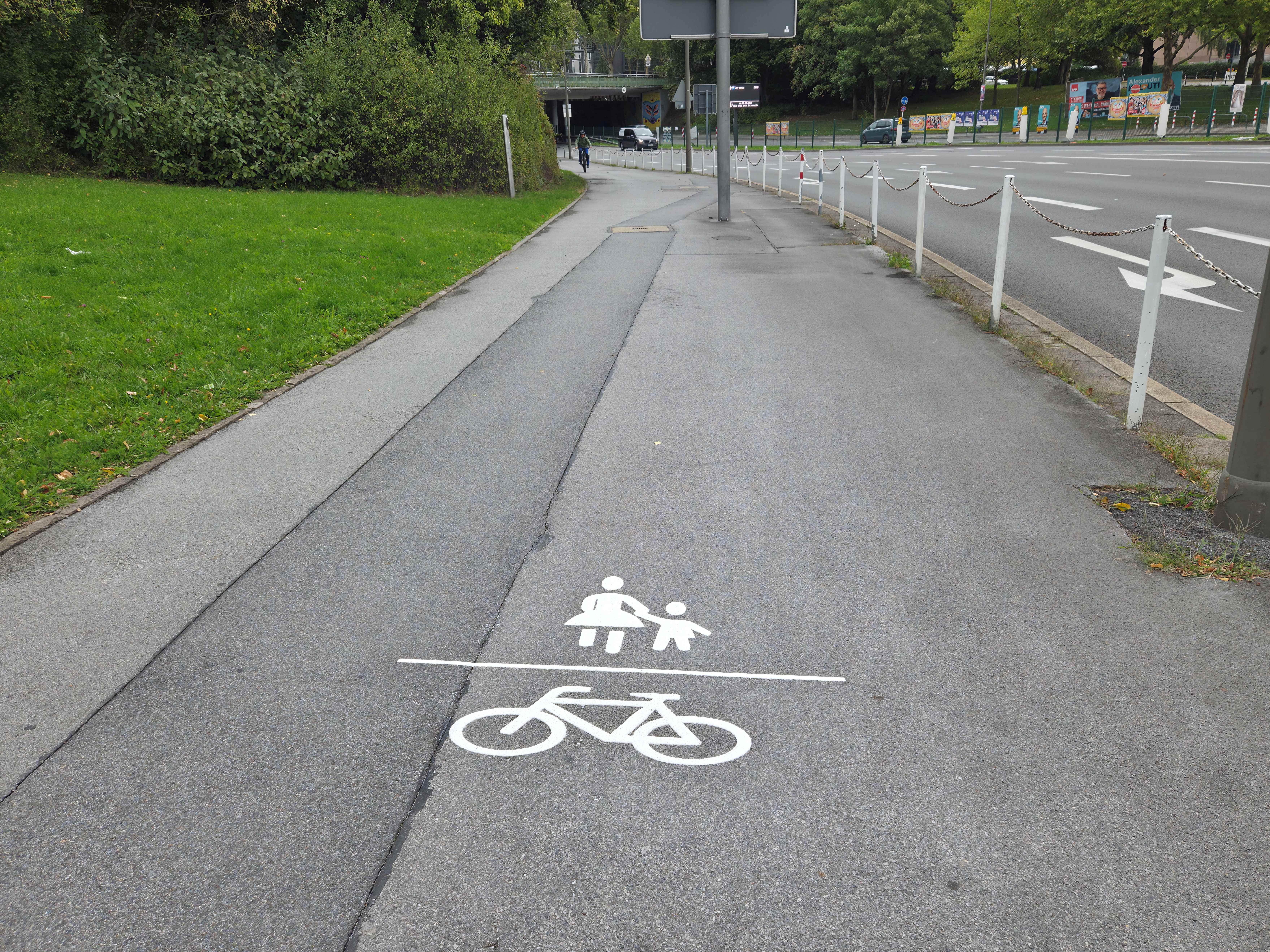 Ein Geh- und Radweg mit einem weißen Fahrrad und Fußgänger Piktogramm in der Mitte. 