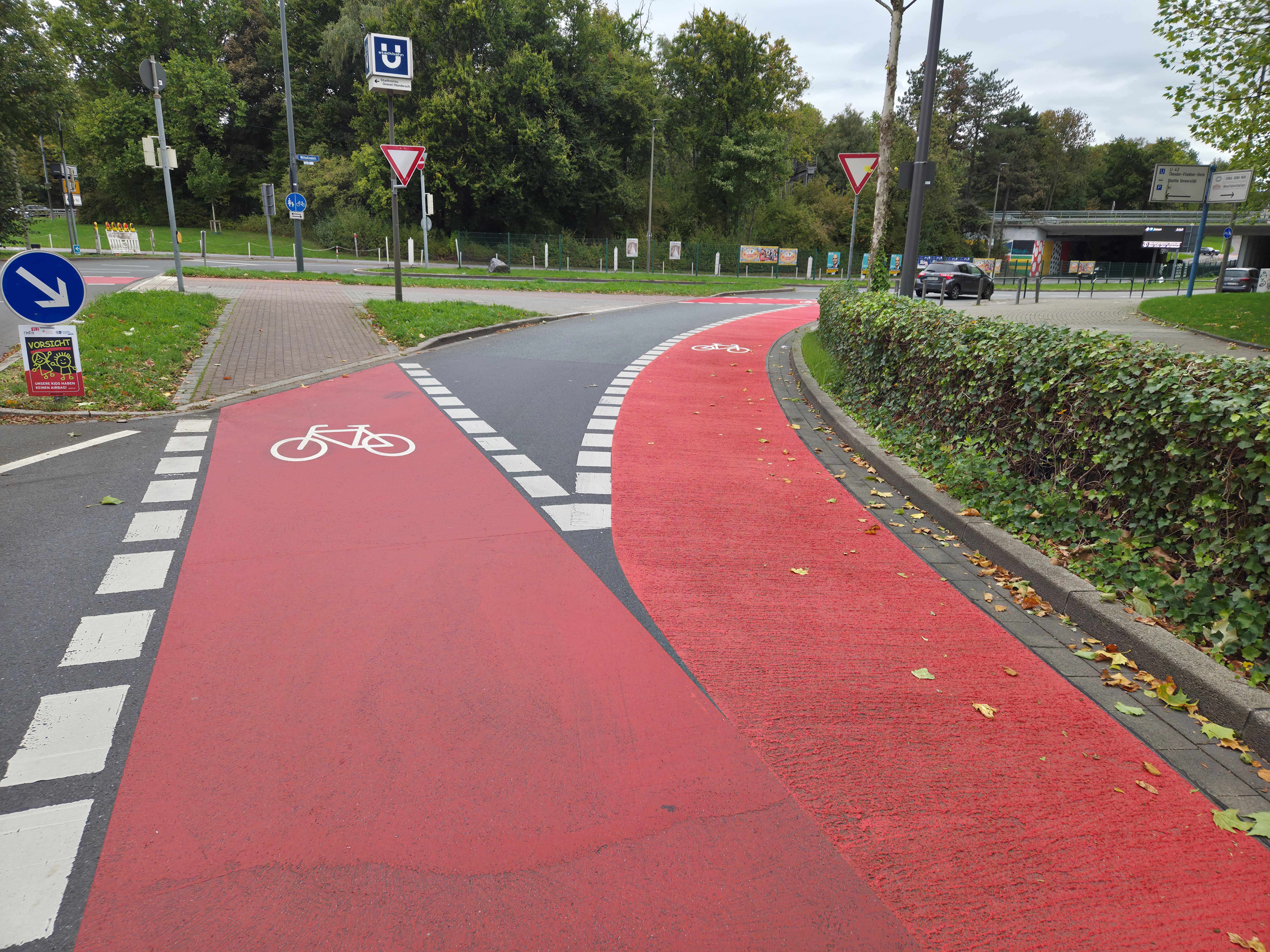 Zwei rote Fahrradfurten mit Fahrradpiktogrammen, an denen Radfahrende nach links oder rechts abbiegen können. 