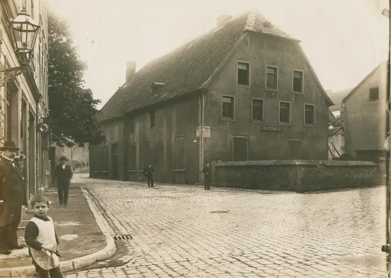 Eisenmarkt 1 vor dem Jahr 1918, ein kleines Kind und ein Mann stehen links auf dem Bürgersteig und schauen in die Kamera, drei weitere Männer stehen im Hintergrund