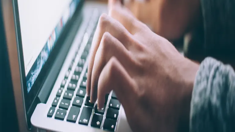 Ein Bild einer Tastatur vor einem Bildschirm, auf dem zwei Hände zu sehen sind.