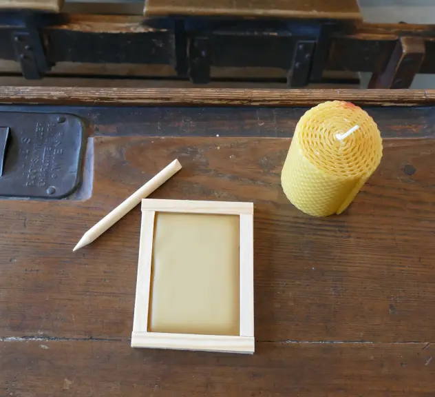 Wachstafel, Stift und Bienenwachskerze auf einem alten Holzschreibtisch