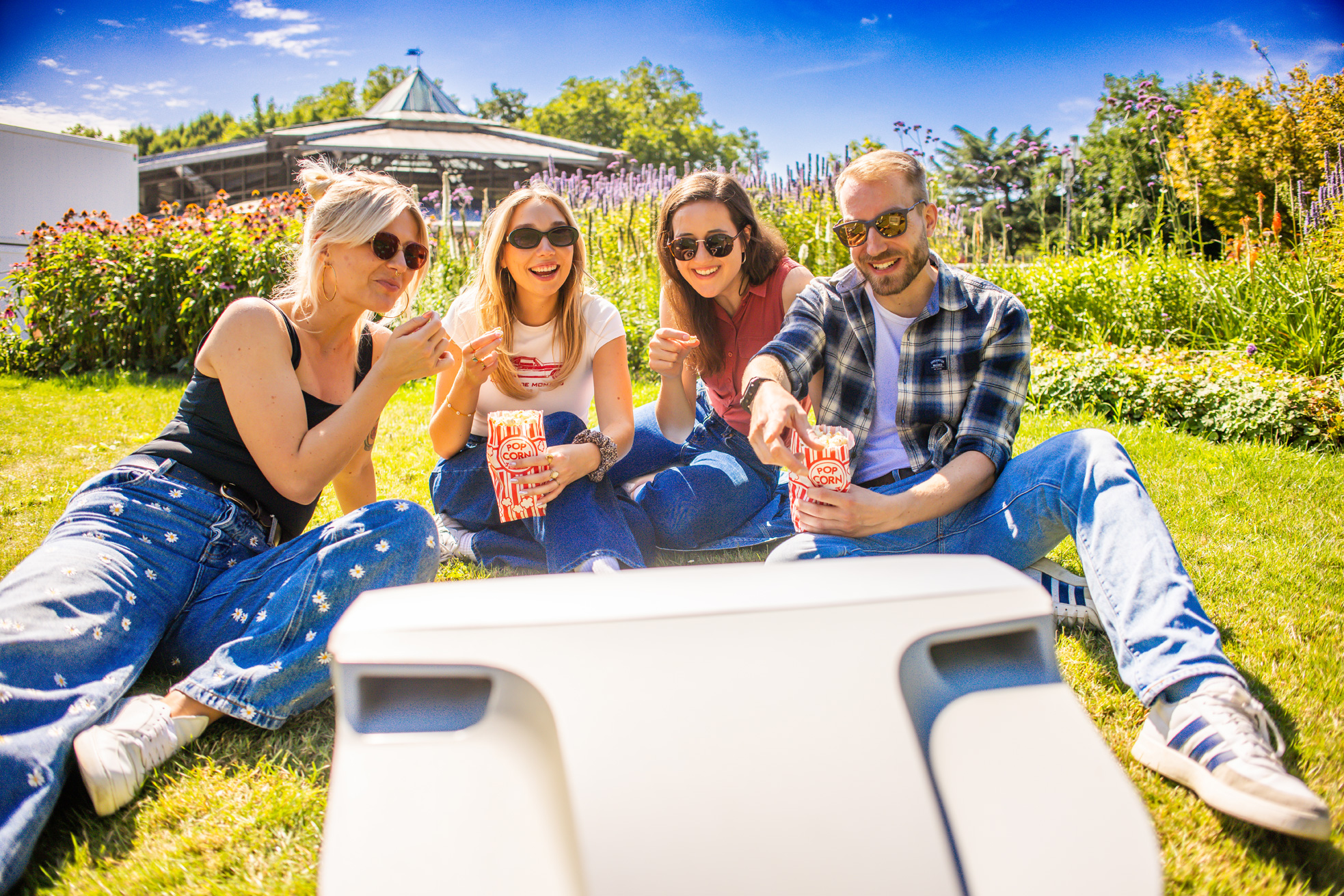 Vier Personen sitzen auf einer Wiese vor einem Fernseher im Stadtgarten.