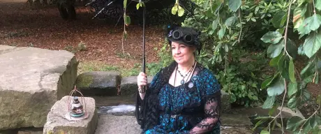 Frau in Steampunk-Kostüm mit Regenschirm sitzt im Park.