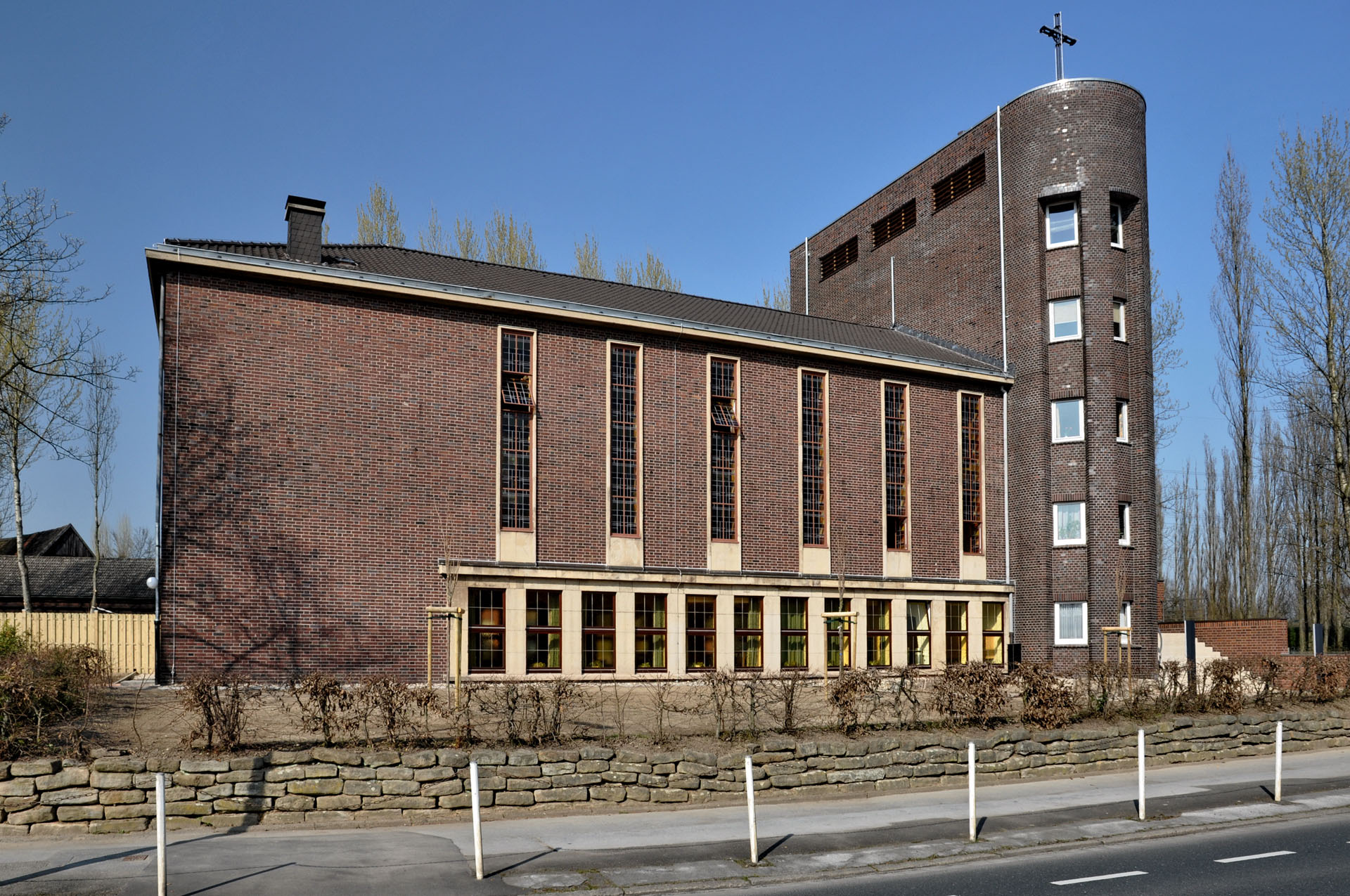 Backsteinkirche im Stil der Neuen Sachlichkeit mit flachem Dach, hohen Fenstern und einem markanten Turm an der Rahmer Straße.